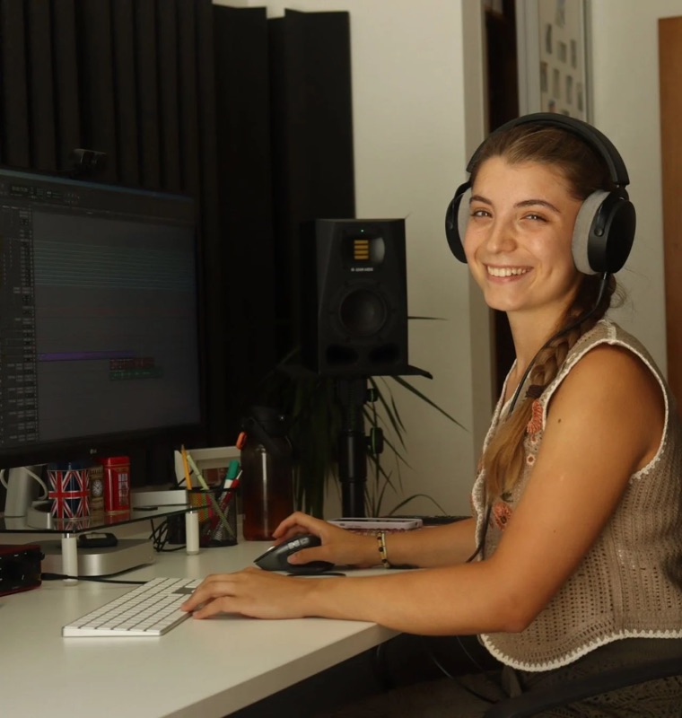 Portrait of Lúcia Carvalho at her desk, wearing headphones.