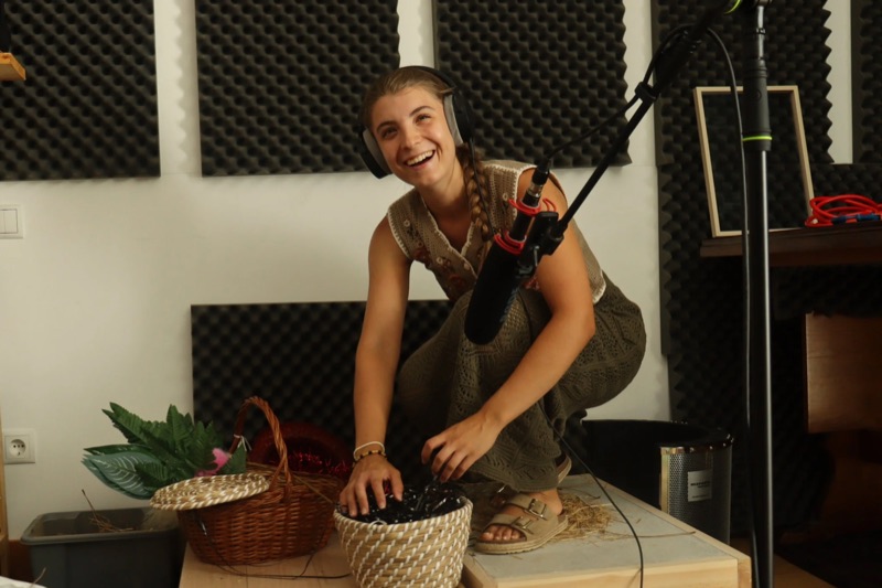 Lúcia Carvalho crouched over a basket of props in front of a boom microphone.